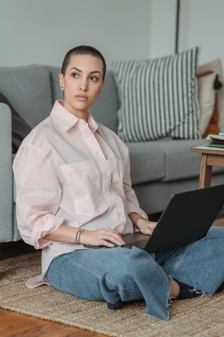 Pensive Woman Sitting On Floor While Working On Laptop In Living Room