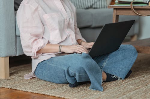 Crop unrecognizable female freelancer sitting on floor and browsing netbook in living room in daytime
