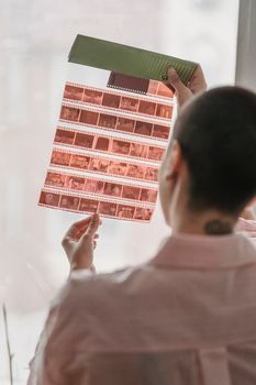 Individual examining a strip of photographic film indoors, emphasizing analog photography.