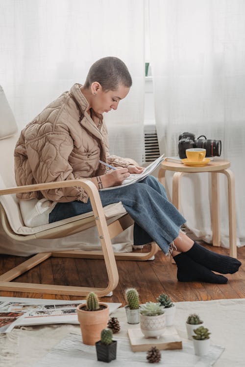 Free A Person in Beige Jacket Sitting on Chair while Writing Stock Photo
