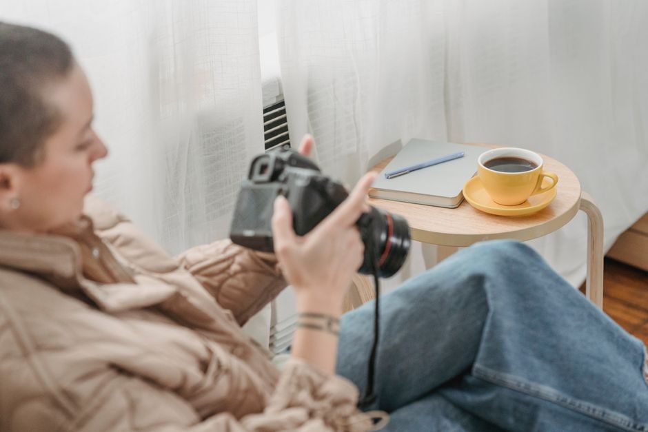 A woman holding a camera sits indoors, with a cup of coffee on a nearby table, capturing a cozy moment.