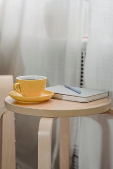 A cozy setup with a yellow coffee cup and notebook on a wooden table, ideal for creativity.