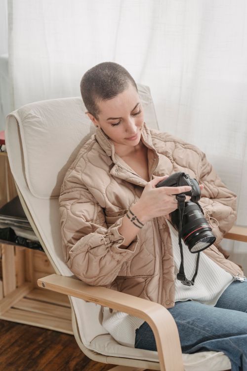 Free A woman with short hair reviews her DSLR camera settings while seated indoors. Stock Photo