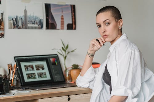 Thoughtful woman with stylus working with photos on laptop