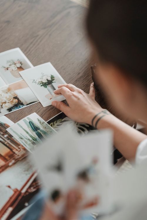 Free From above of crop unrecognizable tattooed person at table with various photos of flower bouquets Stock Photo