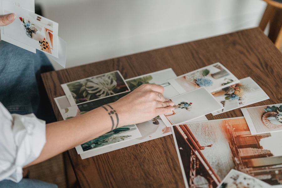 Hands laying out a spread of photographic prints on a wooden table, by George Milton on Pexels