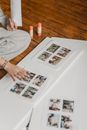 Crop unrecognizable tattooed female compiling photo collage on blank paper while sitting on wooden floor