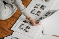 High angle of crop unrecognizable tattooed female compiling photography collage on paper sheet while sitting on floor