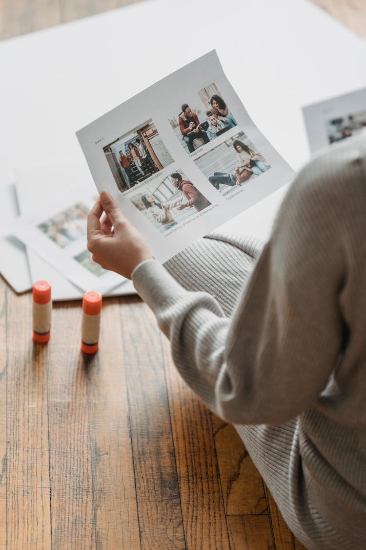 Crop Unrecognizable Person Looking Through Printed Pictures On Floor