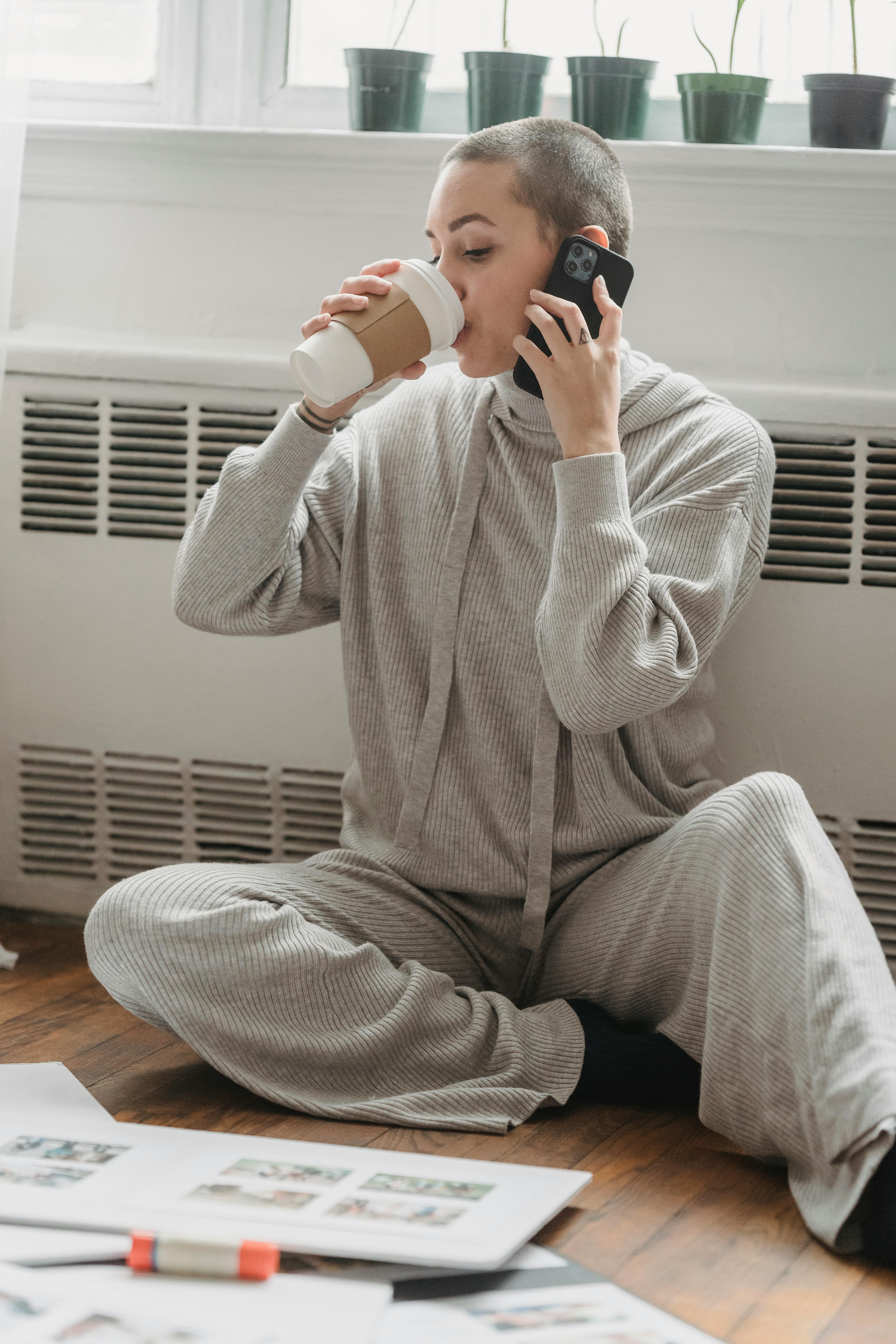 woman drinking coffee and talking on phone near window