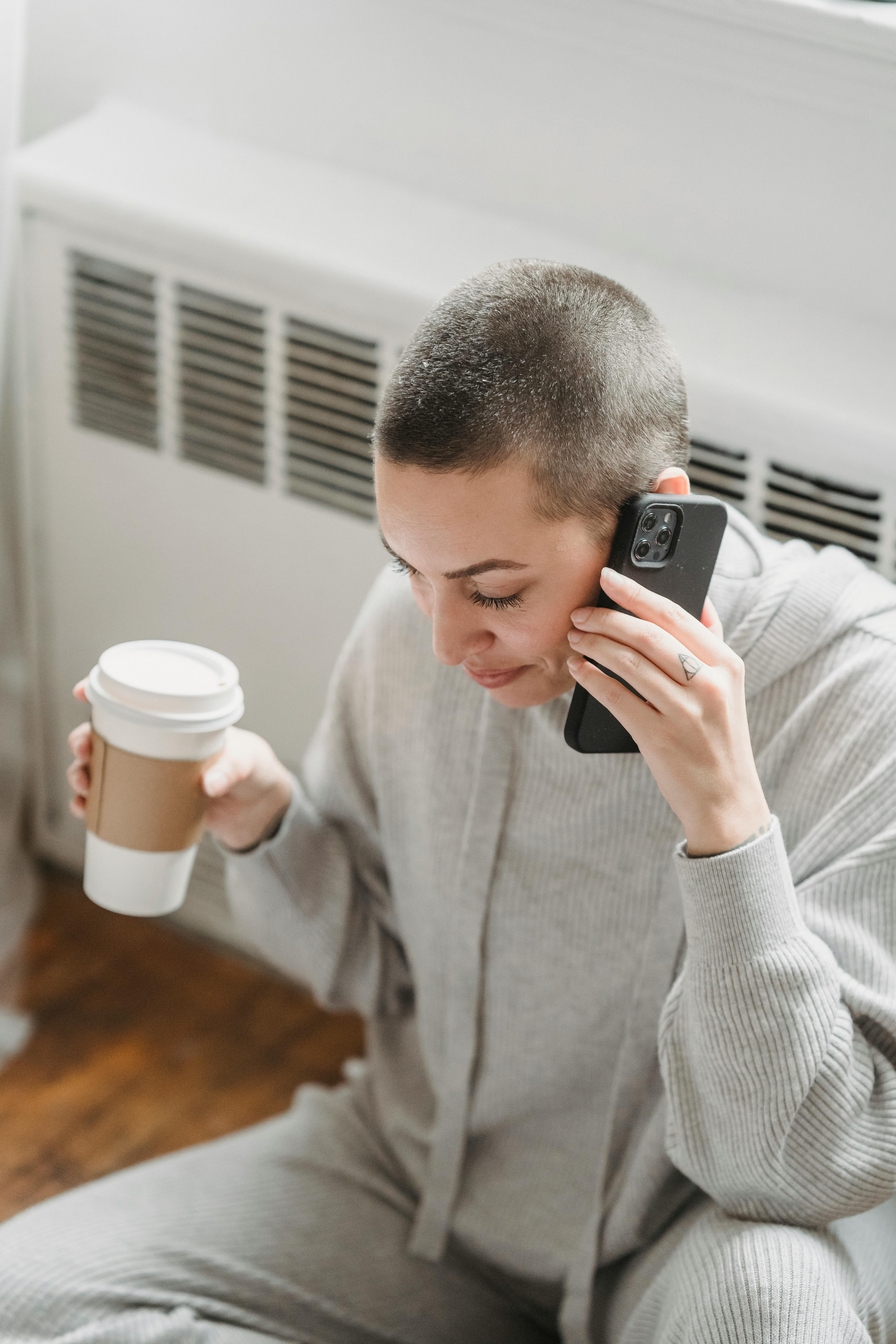 woman with coffee talking on phone near window