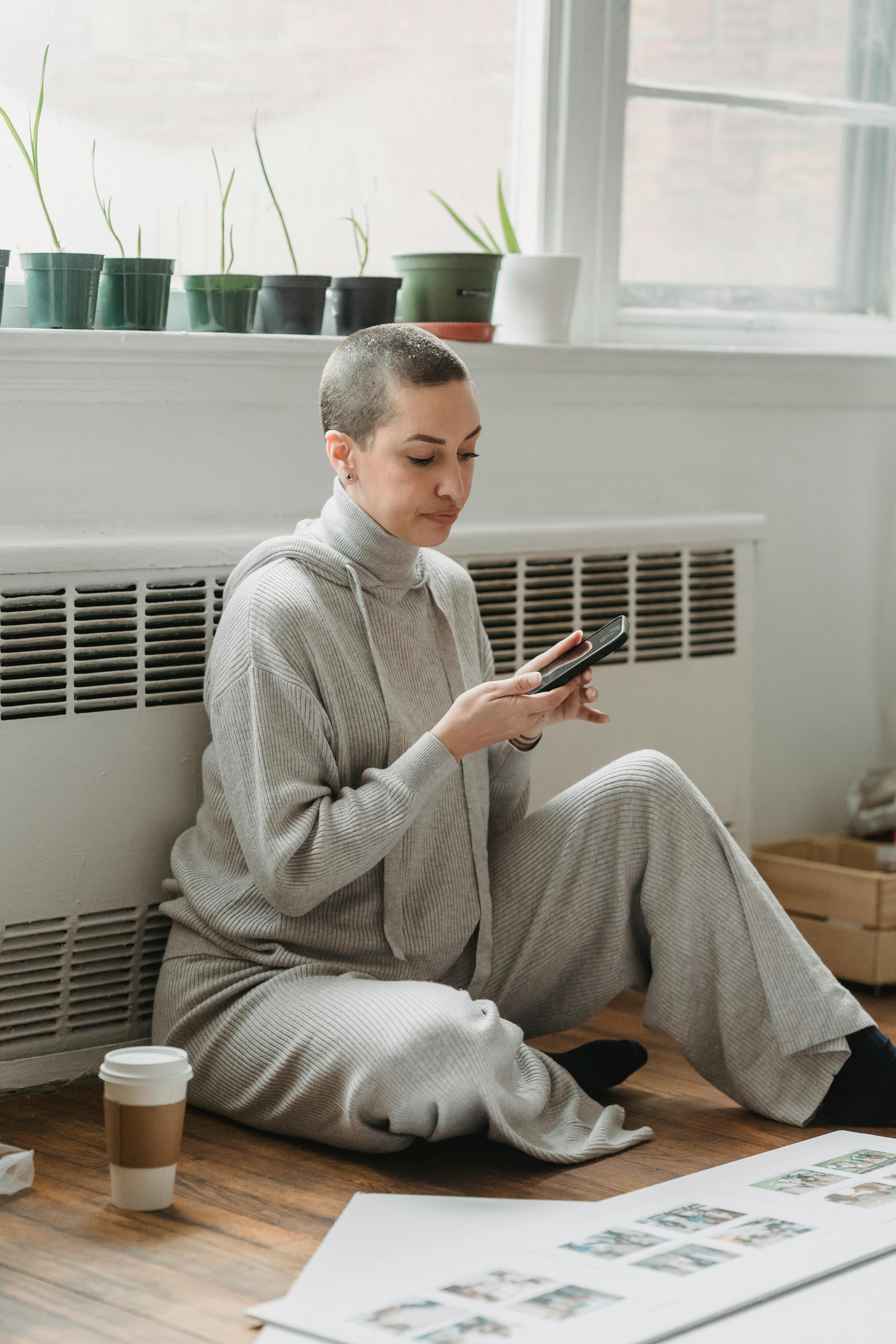 woman texting and sitting on floor near window