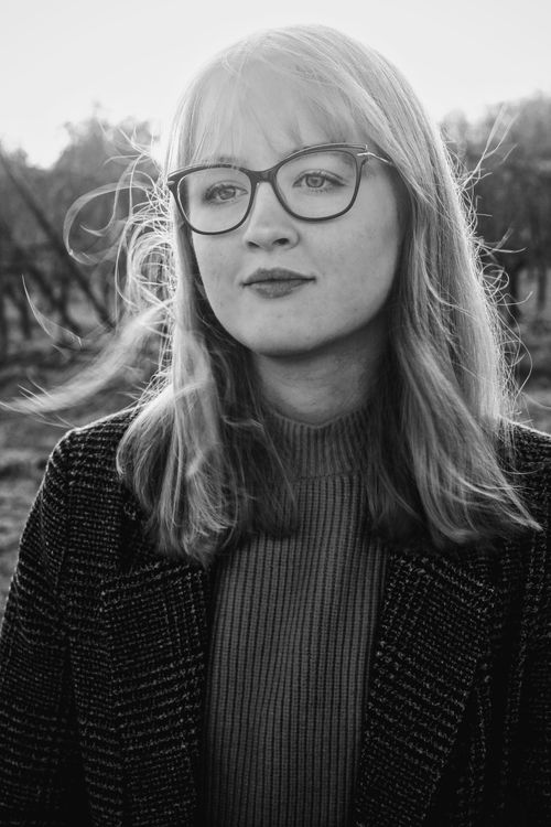 Free Black and white portrait of a woman wearing glasses in an outdoor setting, emphasizing her thoughtful expression. Stock Photo