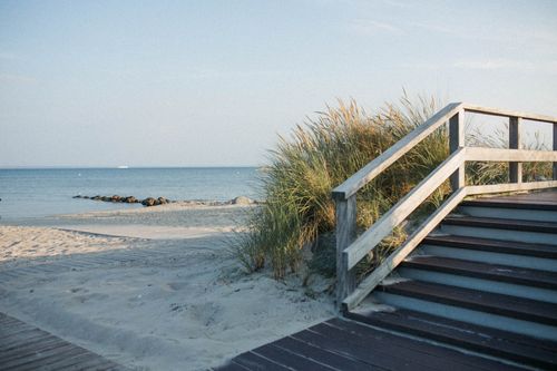 Free Scenic view of a wooden pathway leading to a tranquil sandy beach with gentle ocean waves. Stock Photo