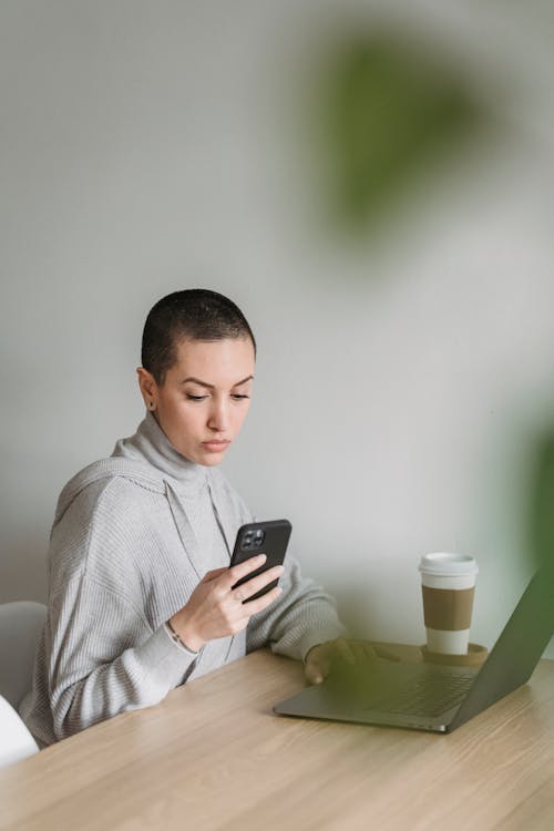 Focused woman using smartphone and working on laptop