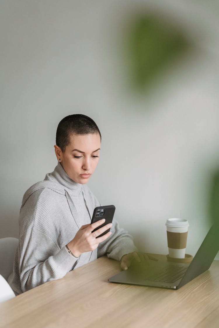 Focused Woman Using Smartphone And Working On Laptop