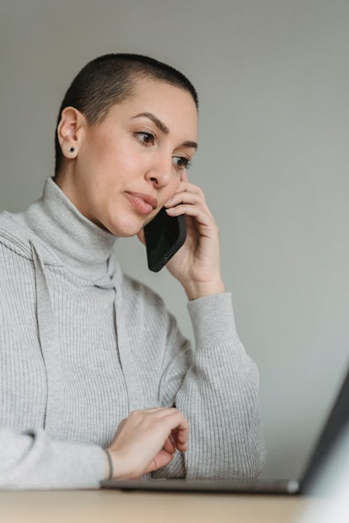 Thoughtful woman talking on smartphone and working on laptop