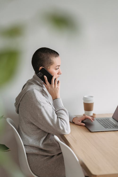 Free Focused woman talking on phone and using laptop Stock Photo