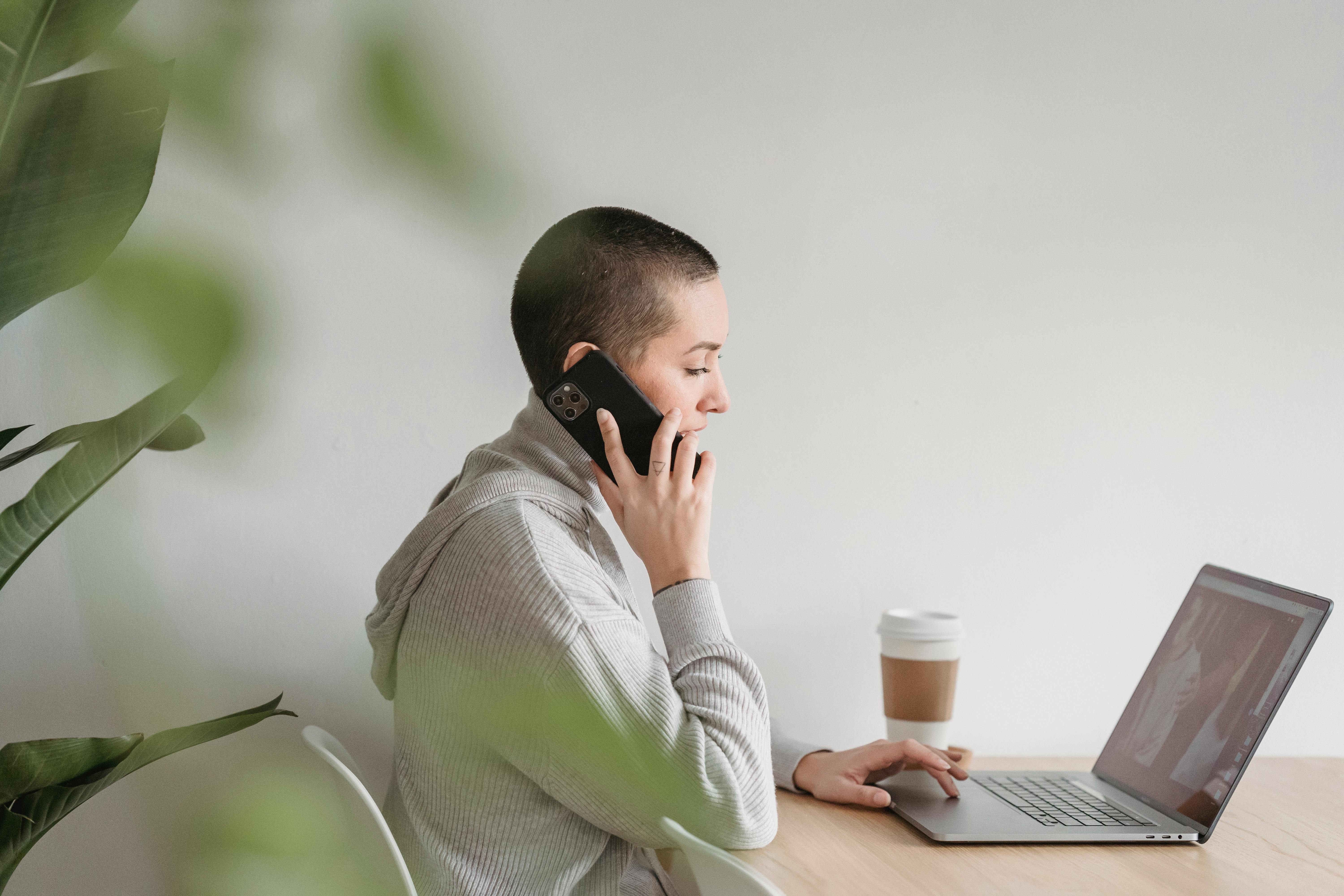 woman talking on smartphone and working on laptop at home