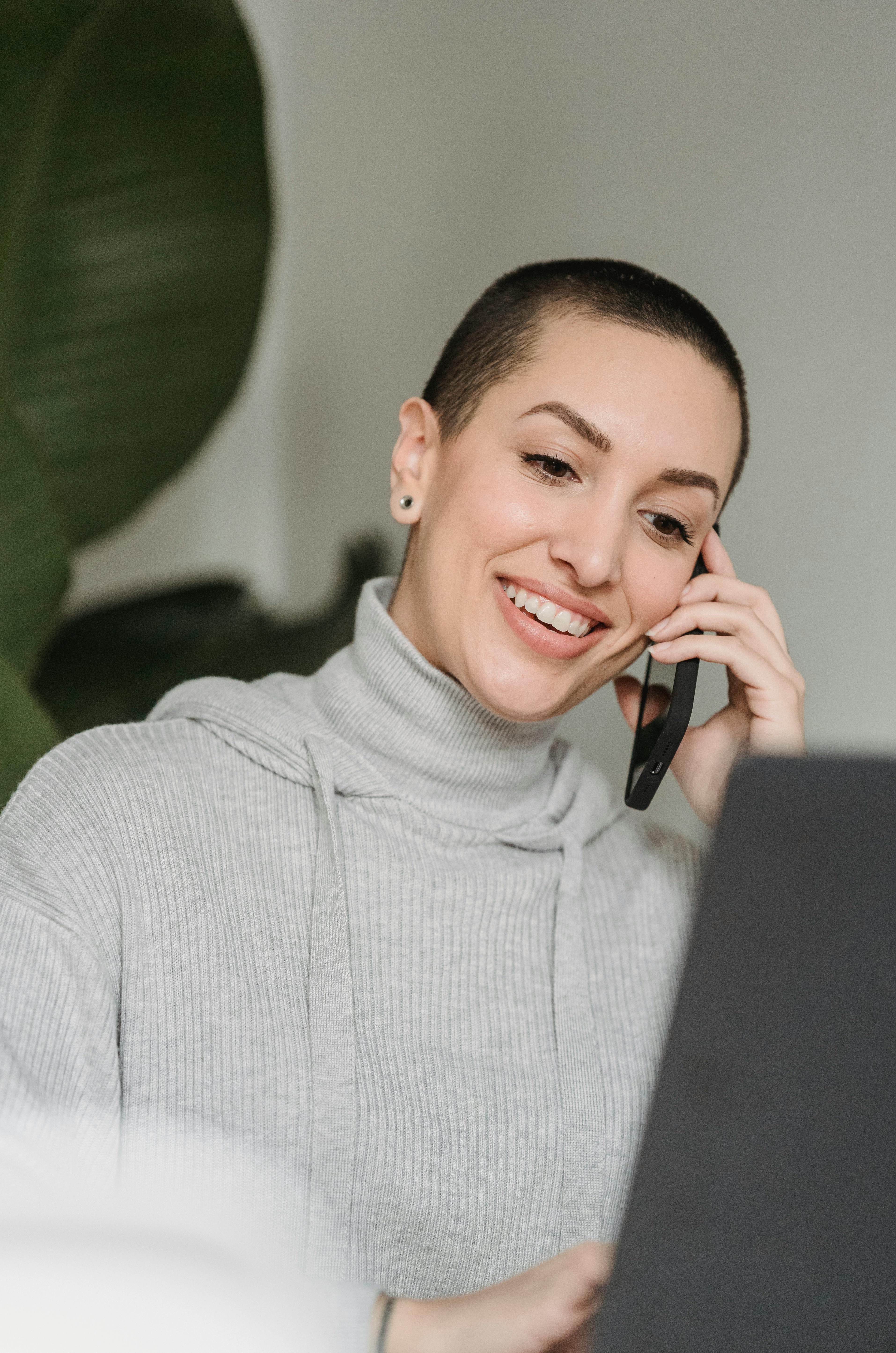 smiling woman talking on smartphone and working on laptop