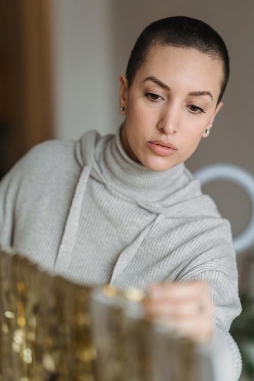 Young contemplative female with short hair hanging shiny golden tinsel on white stand