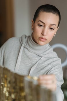 Young contemplative female with short hair hanging shiny golden tinsel on white stand