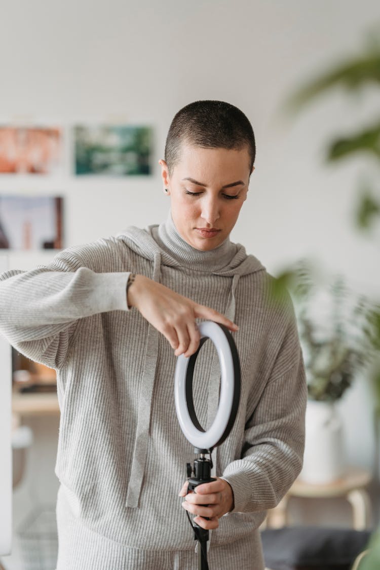 Woman In Hoodie Setting Up Ring Lamp At Home