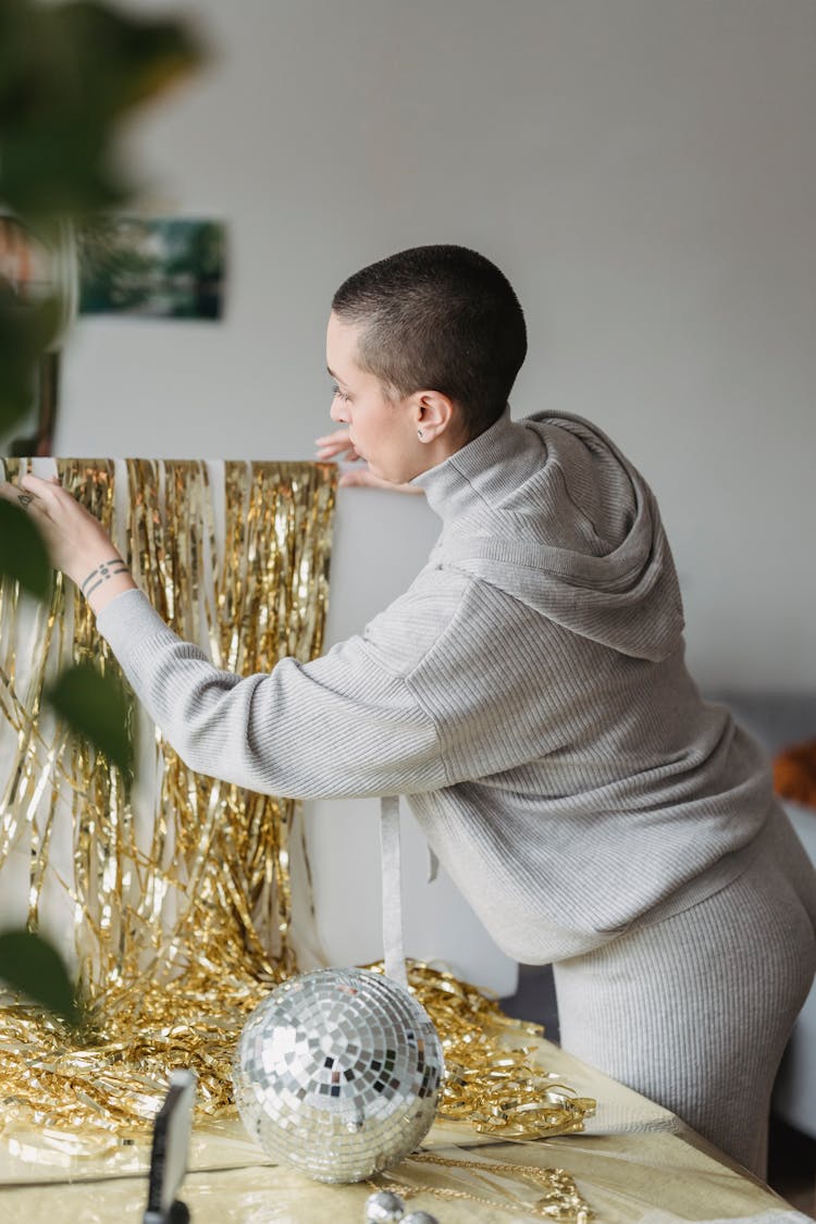 Woman Touching Tinsel At Table With Decorative Ball At Home