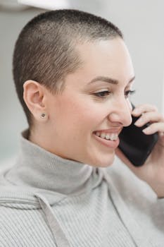 A cheerful young woman with short hair smiling during a phone call indoors.