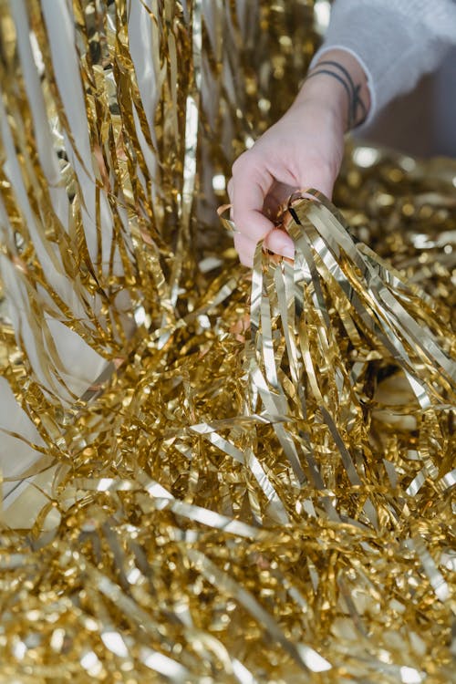 Crop unrecognizable person with tattoo in form of bracelets demonstrating heap of shiny tinsel on blurred background