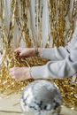 Crop unrecognizable person with tattoos and heap of shiny tinsel against decorative ball indoors