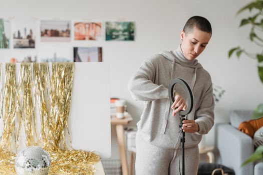 Attentive woman setting up ring lamp against tinsel at home