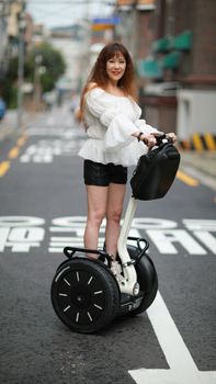 Woman in black shorts and off-shoulder top riding Segway on a city street, smiling. — photo by 거열 박