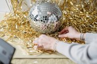 Crop woman at table with shiny tinsel and decorative ball