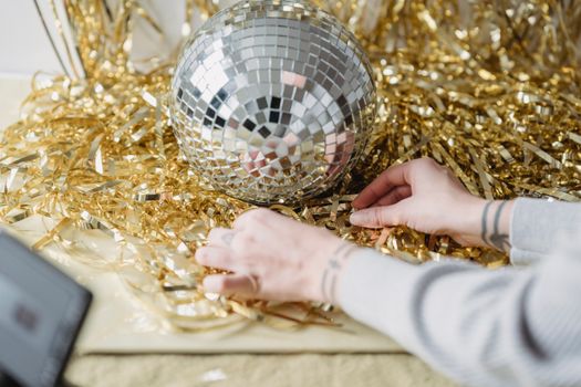 Crop woman at table with shiny tinsel and decorative ball
