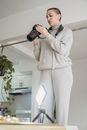From below of young woman taking photo on professional camera against glowing lamp on table at home
