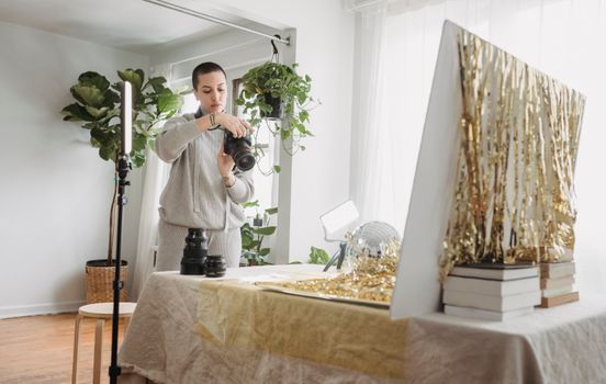 Serious woman reviewing pictures on photo camera while standing near table with golden tinsel and party ball