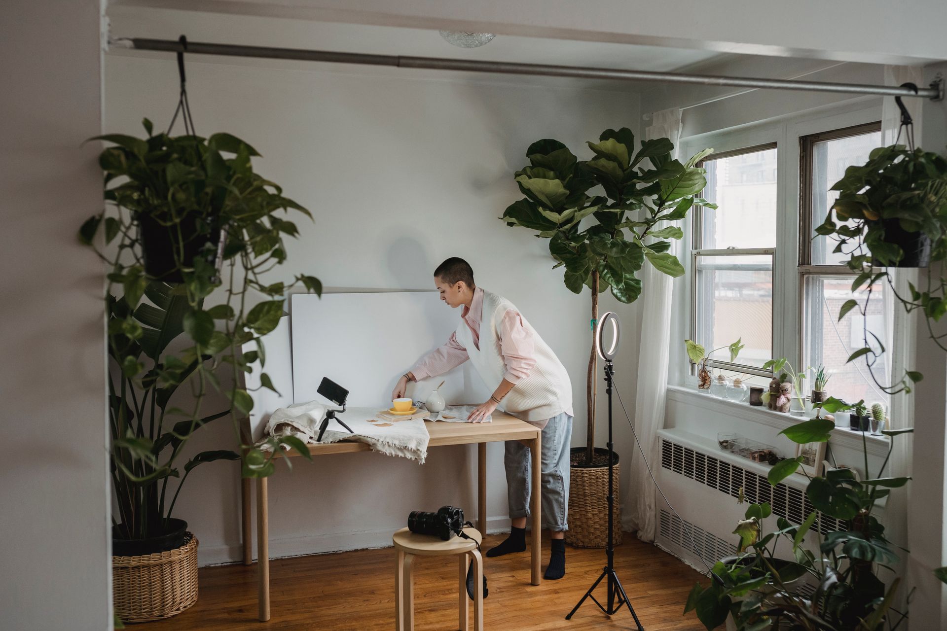 Full body side view of busy female photographer preparing equipment for photo session in studio with potted plants and ring light