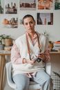 Tattooed female with old photo device sitting in armchair while looking at camera against desk at home