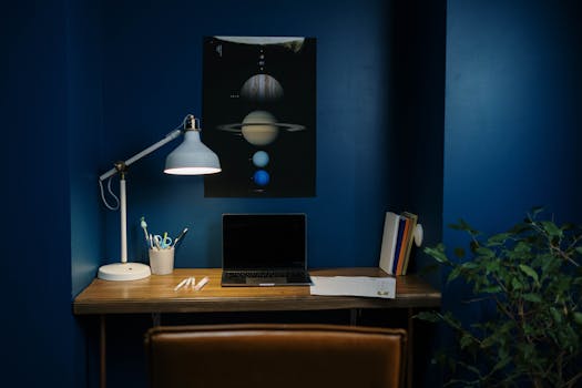 A modern home office with blue walls, desk lamp, and open laptop, creating a focused workspace.