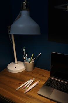 Cozy workspace setup with a desk lamp, laptop, and office supplies on a wooden table.