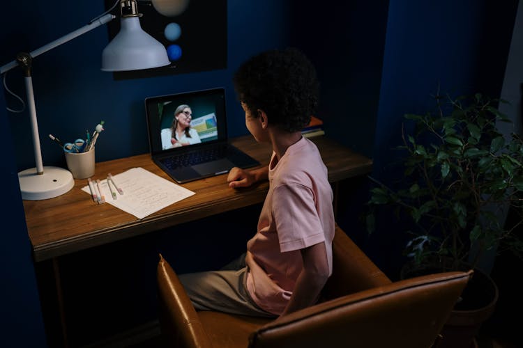 A Boy Home Schooling With A Laptop On A Wooden Desk