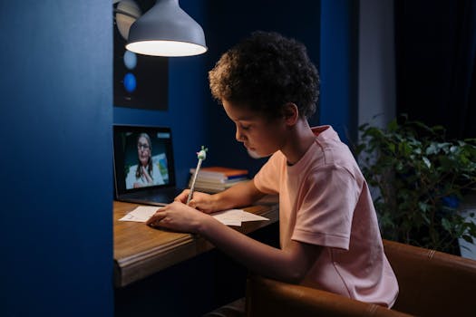 A child focused on online learning with a laptop and papers at a home desk.