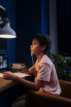 A child focusing on an online lesson at home, under a desk lamp.