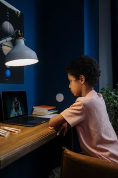 A young student engaging in online learning on a laptop in a warmly lit room.