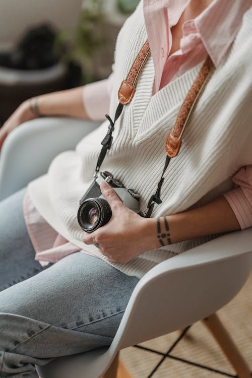 Crop photographer with retro photo camera resting in armchair indoors