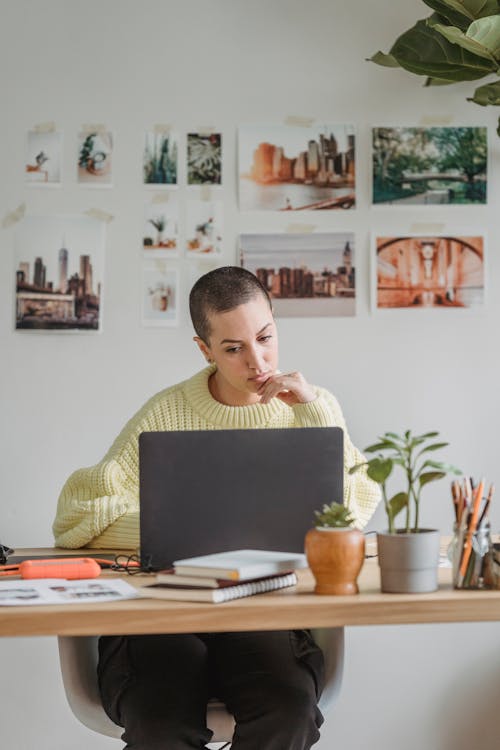 Contemplative young female with short hairstyle using netbook and sitting at desk with papers in light room