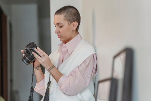 Concentrated young female with short hair looking through pictures in professional photo camera in light studio