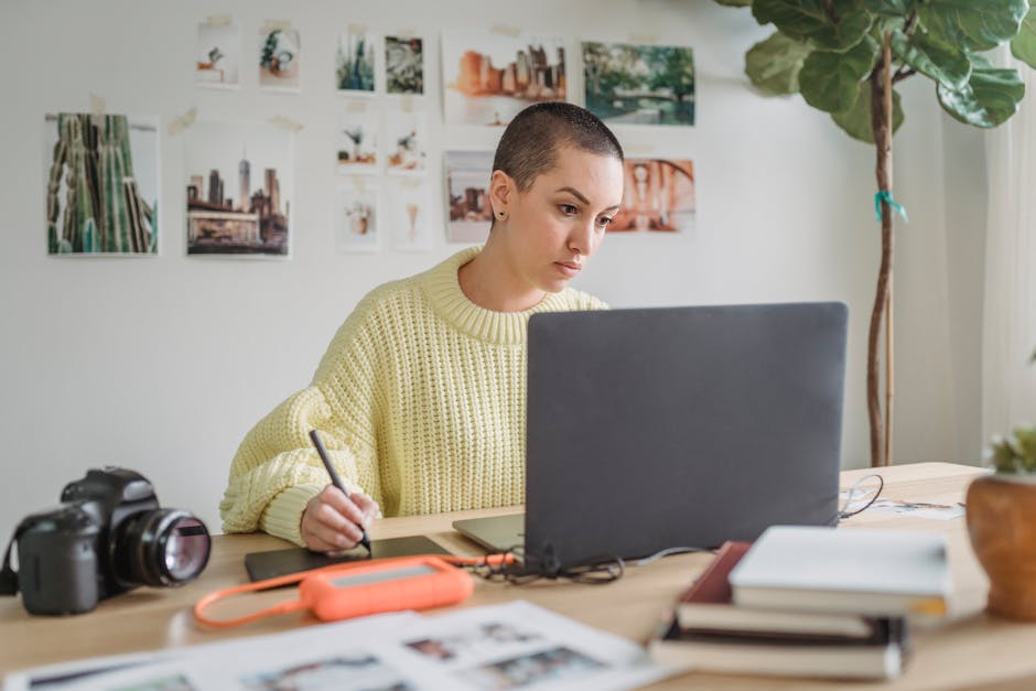 Thoughtful female in casual sweater working on netbook and drawing on graphic tablet in light room