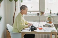 Side view of concentrated female with short hair editing photos on netbook while sitting at table with photo camera in light room